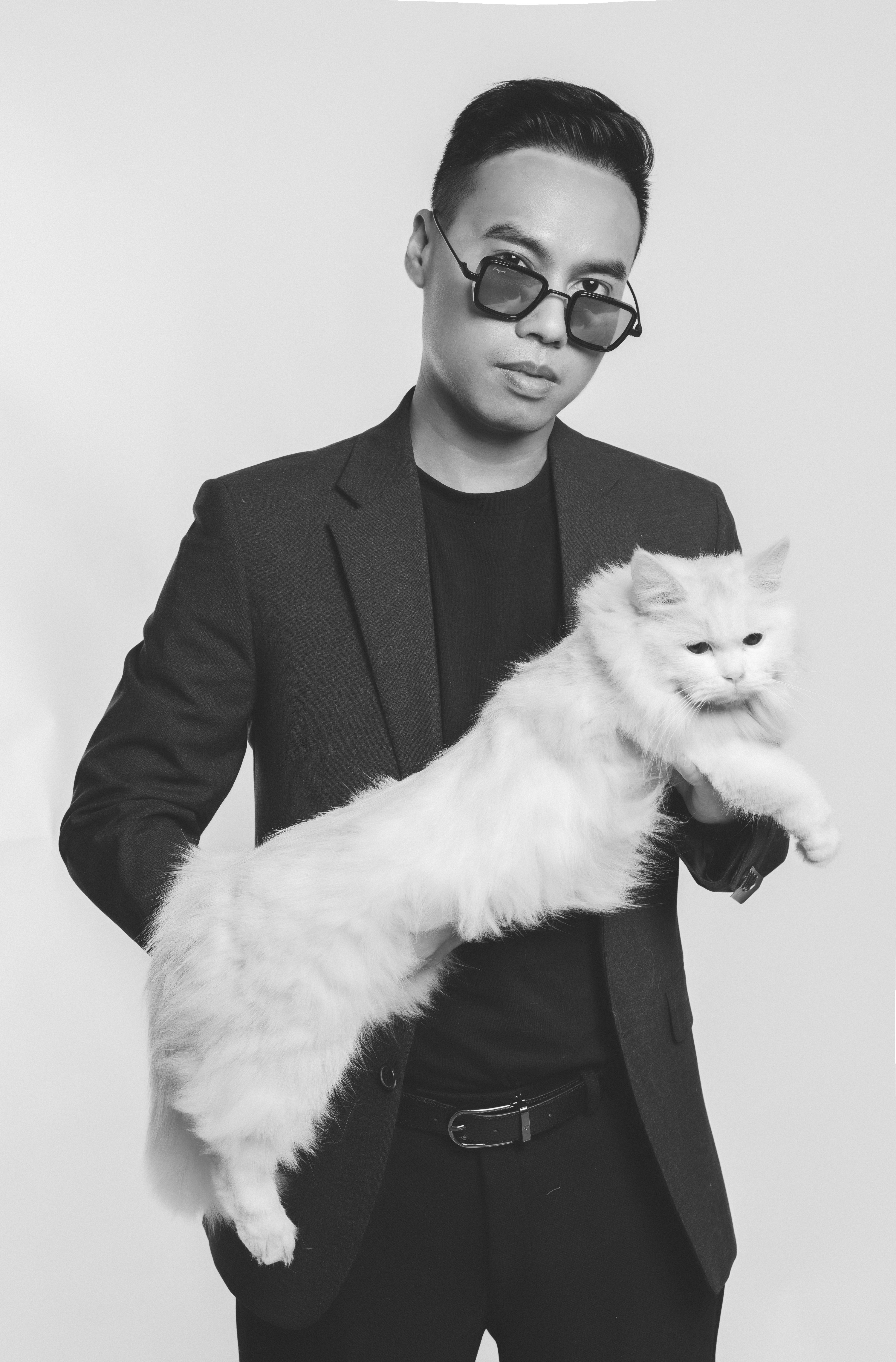 Stylish man in sunglasses holding a fluffy white cat, showcasing elegance and style.