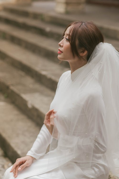 A Woman in White Long Sleeve Dress Sitting while Wearing a Veil