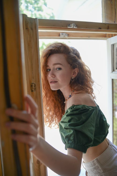 A Woman in Green Off Shoulder Top Near the Wooden Window