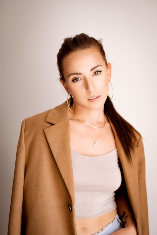 Free Stylish portrait of a woman wearing a brown blazer with gold accessories, indoors. Stock Photo