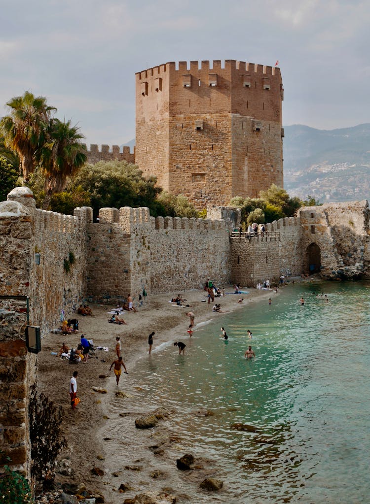 People Relaxing On Beach Under Medieval Fortification Wall