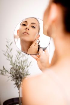 A woman gazes at her reflection in a hand mirror, embodying elegance and self-awareness indoors.