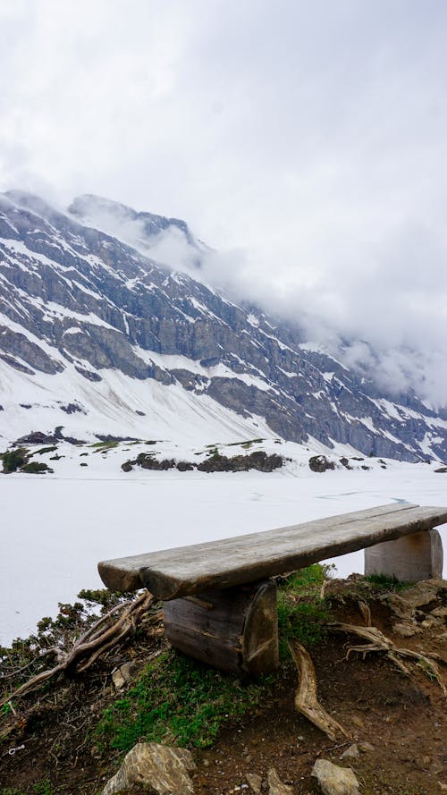 A Wooden Bench Near the Snow Covered Mountain Under the White Clouds