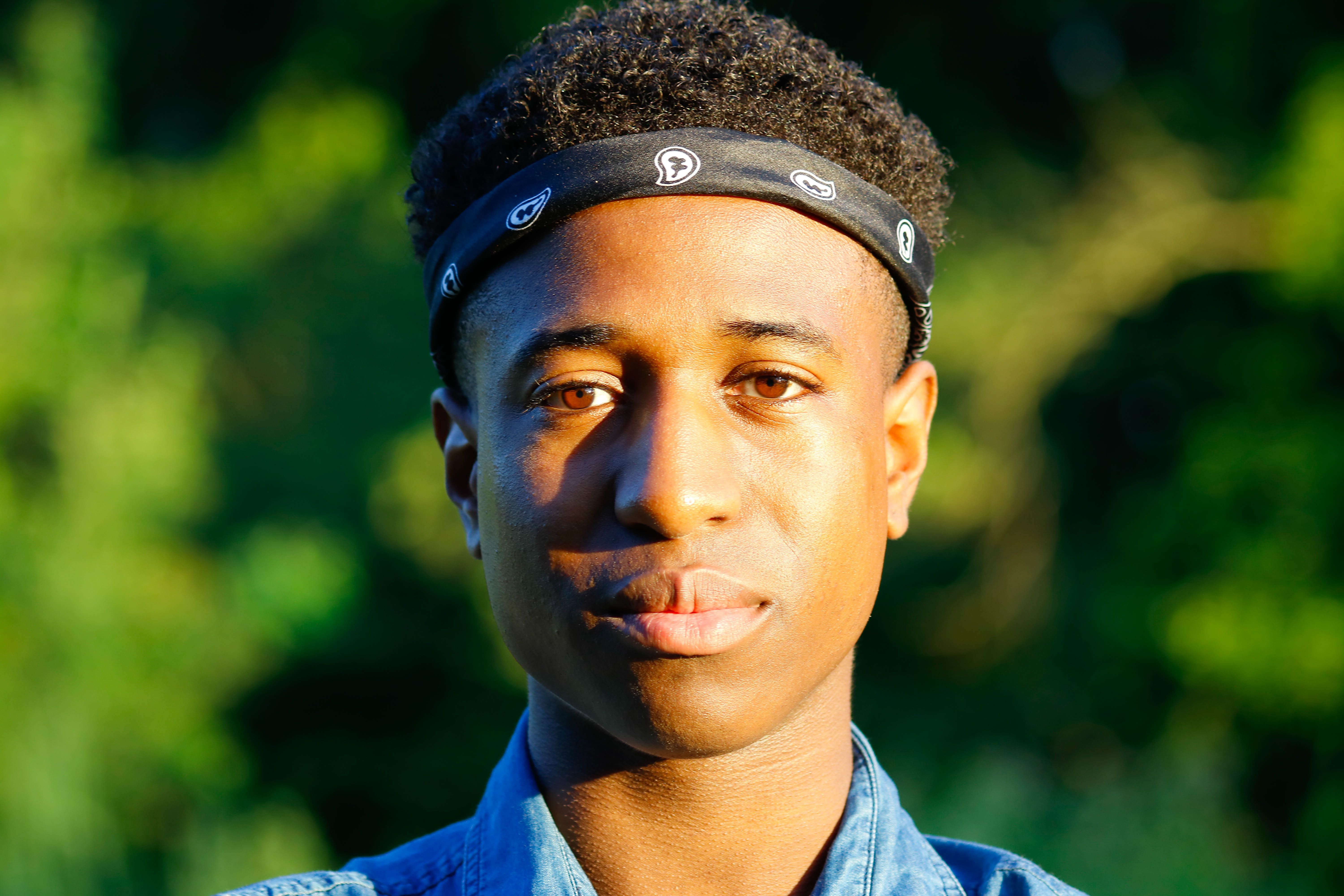 Inspiring close-up of a young black man in a denim shirt, outdoors with sunlight.