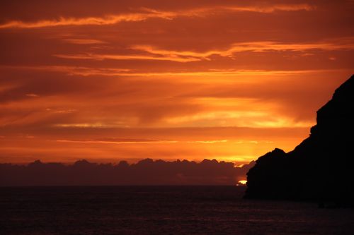 Free Silhouette of cliffs against an intense orange sunset over a calm ocean. Stock Photo