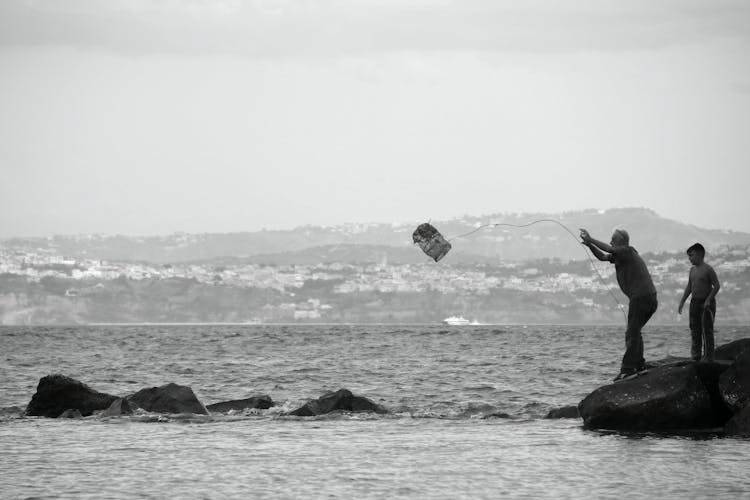 Black And White Photo Of A Man And A Boy Fishing With A Net