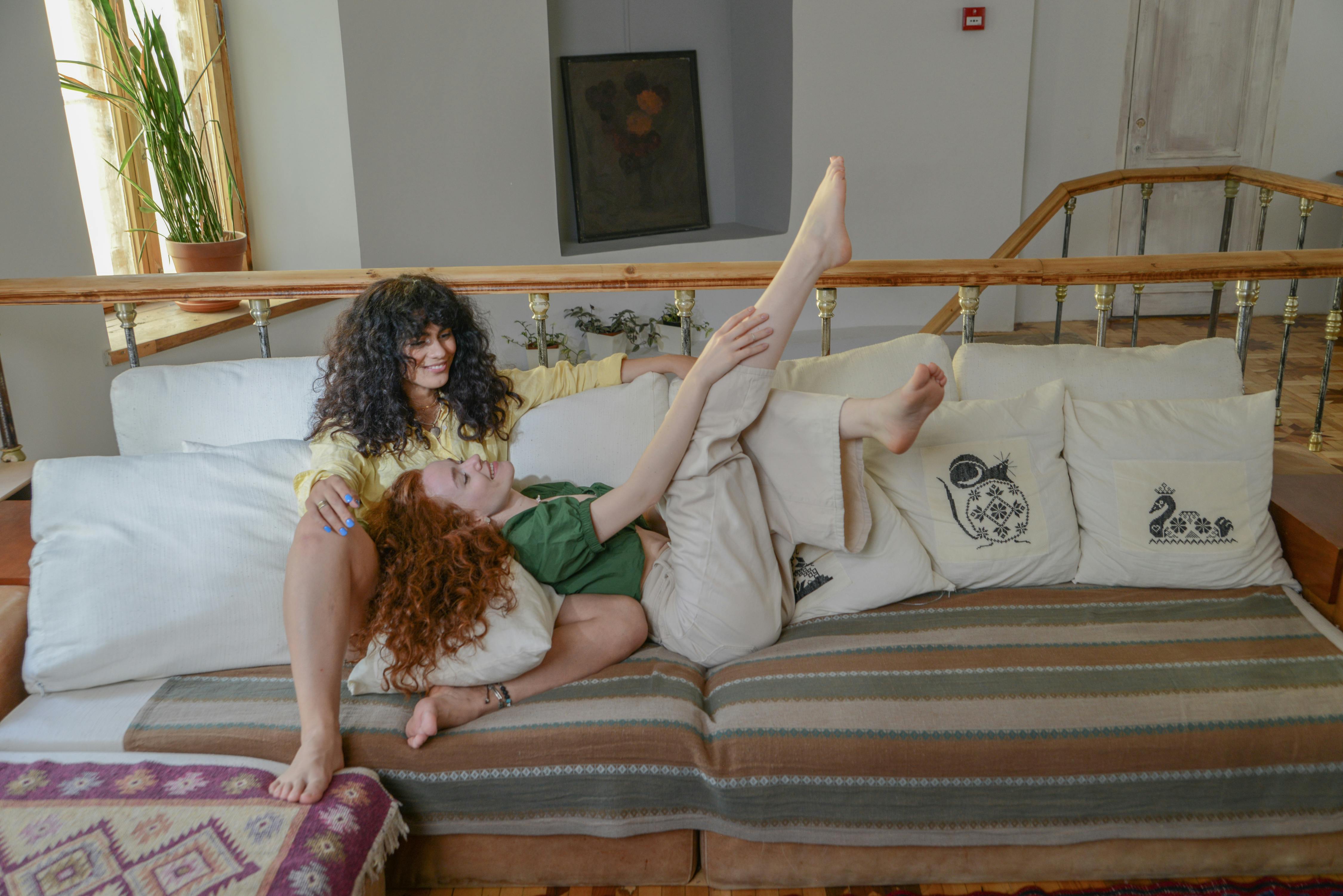 Two women enjoying a playful moment on a comfortable couch, showcasing warmth and friendship.