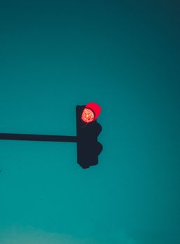 A striking red traffic light against a clear turquoise sky in New York City, symbolizing urban safety.