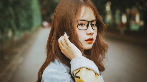 Free Close-up of a young woman with glasses in a stylish jacket outdoors with a blurred background. Stock Photo