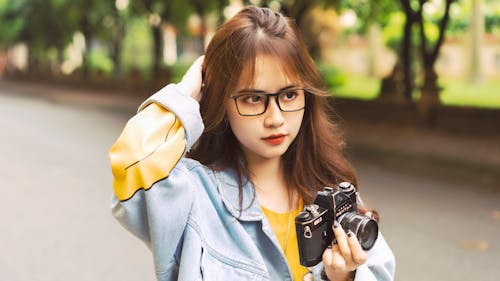Close-Up Shot of a Pretty Woman with Eyeglasses Holding a Camera 