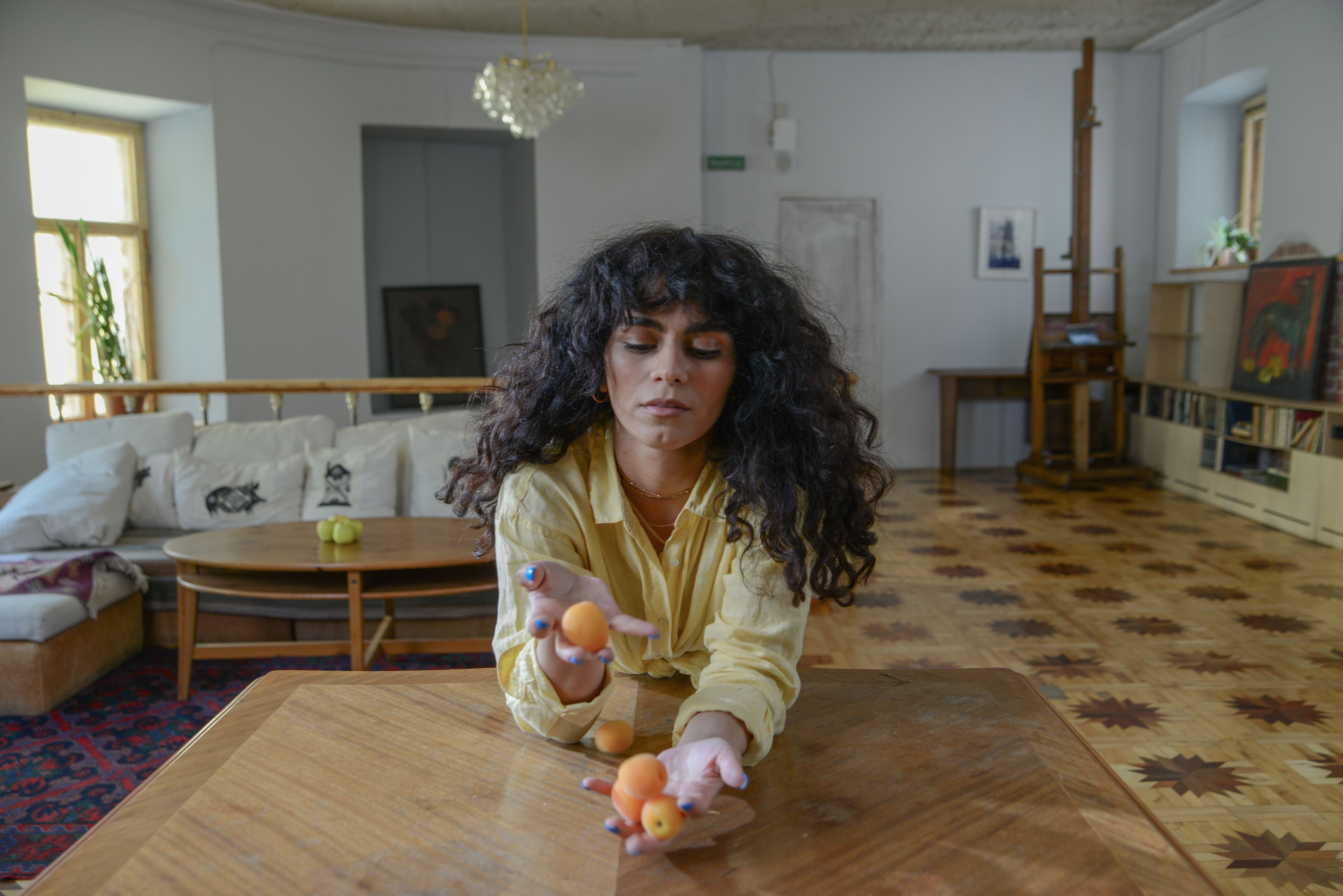 A woman skillfully juggles apricots in a chic, well-furnished living room with a wooden floor.