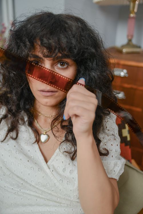 Free A woman with curly hair closely examines a film strip in a cozy indoor setting. Stock Photo