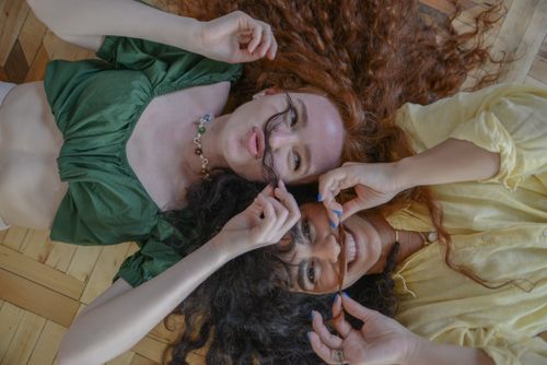 Free Two women with curly hair lying on wooden flooring, enjoying playful moments and happiness. Stock Photo