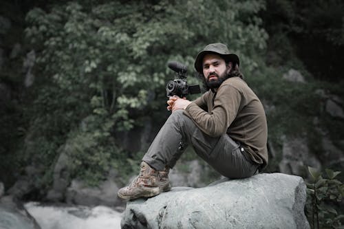 A Man Sitting on a Rock While Holding a Camera 