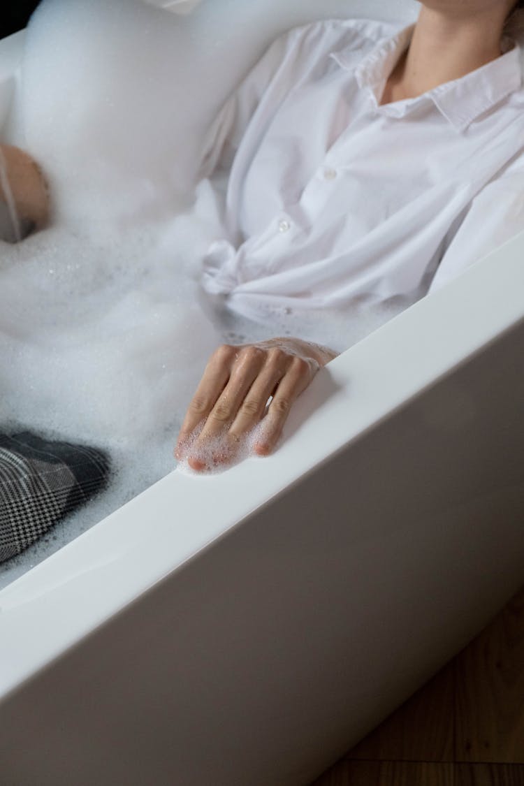 Person In White Long Sleeves Soaking On Bathtub