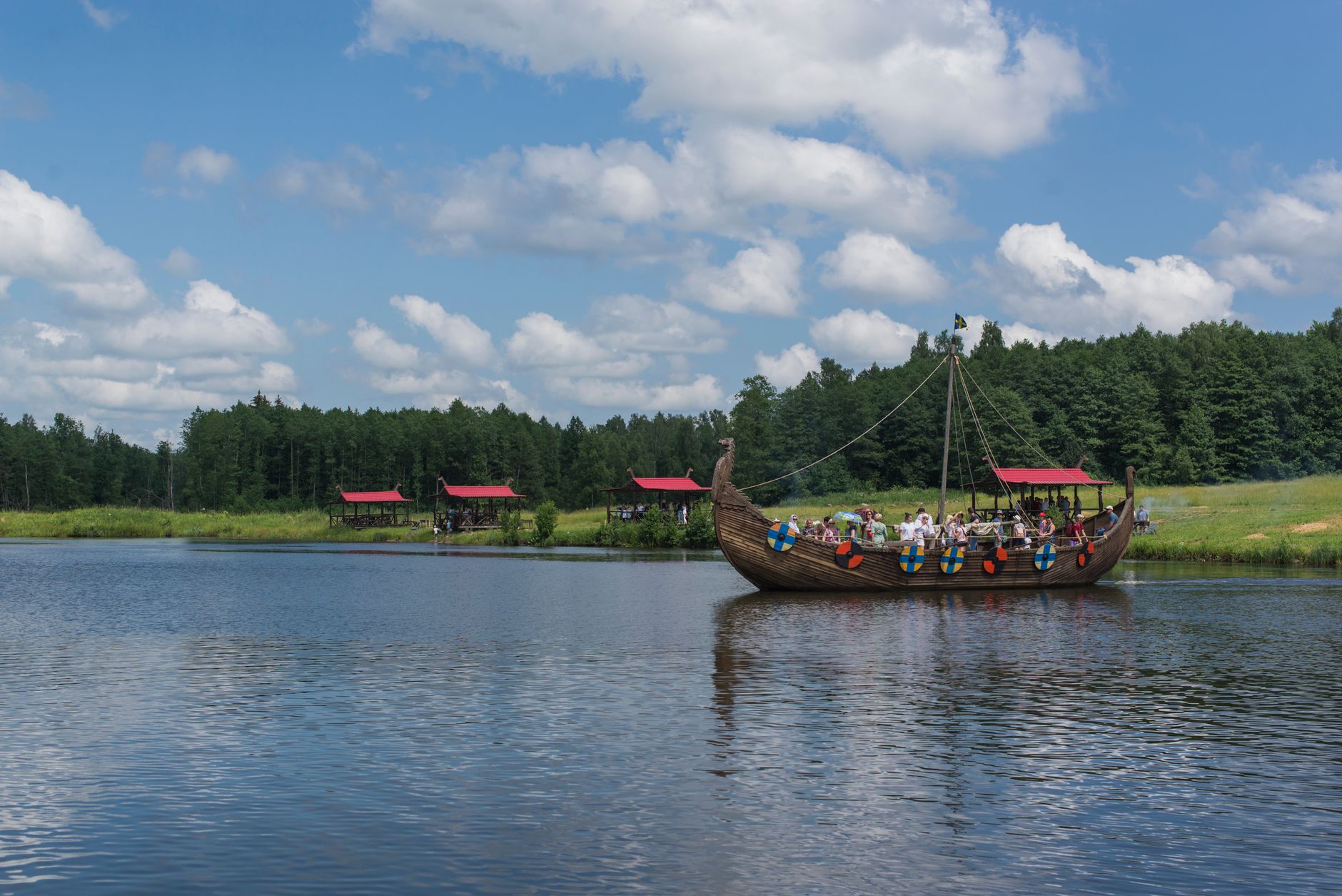 A Viking-style ship sailing on a tranquil lake with people enjoying the scenic summer view in Belarus.