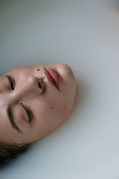 Close-up of a woman with eyes closed submerged in a milky bath, evoking a sense of tranquility.
