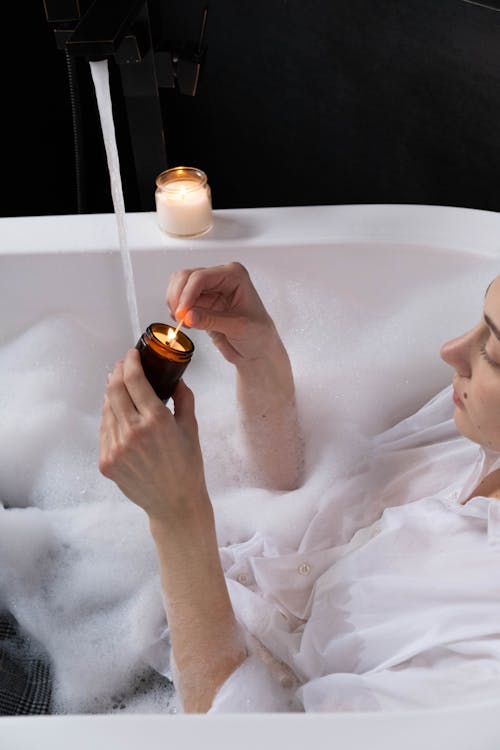 A Woman Resting on the Bathtub while Lightning the Candle on a Jar