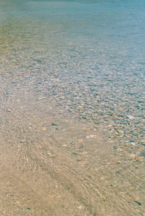 Free Serene view of clear water lapping over pebbles in Mykonos, Greece, perfect for relaxation and calmness. Stock Photo