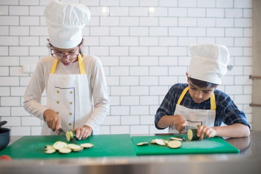 A Young Girl and Boy Slicing Vegetables while Wearing Apron