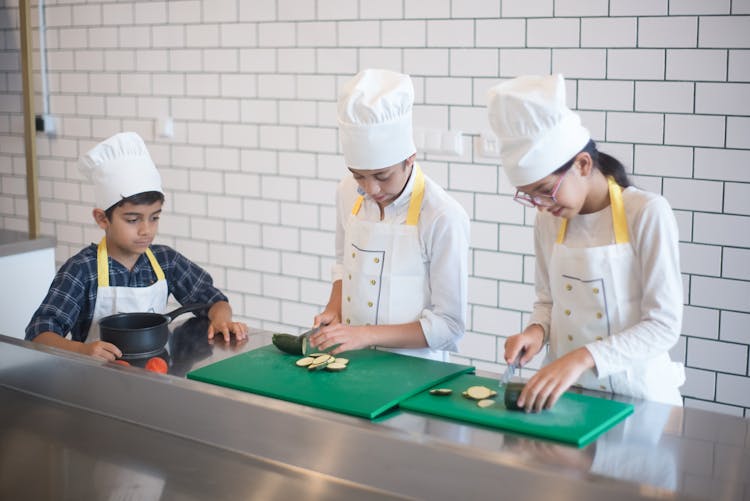 Young Kids Wearing Aprons While Slicing Vegetables