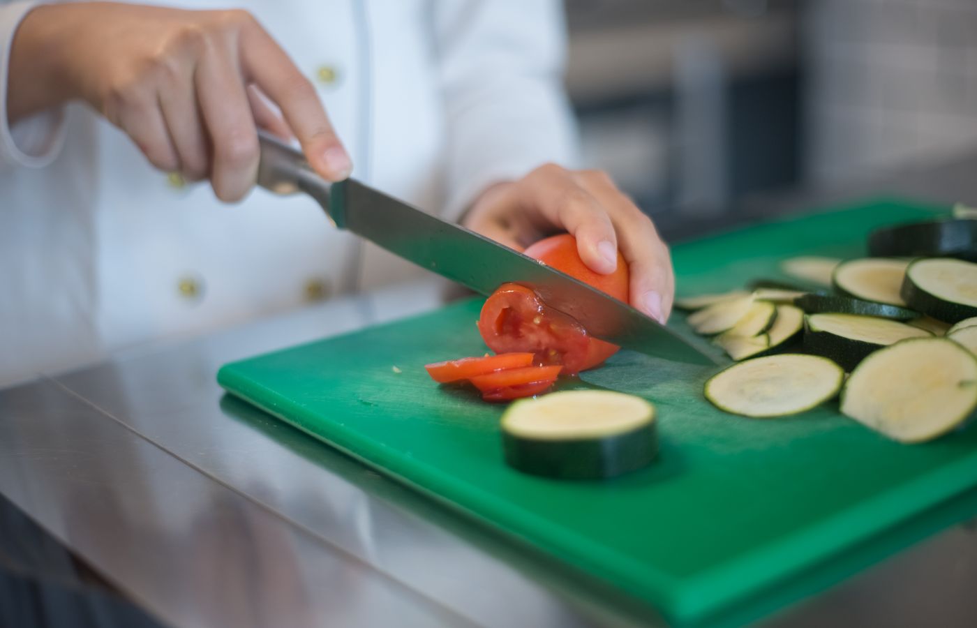 Chef precisely slices tomato and zucchini on green board, enhancing culinary presentation.
