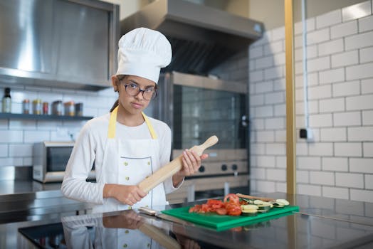 A young girl in a chef outfit prepping vegetables in a modern kitchen setting.