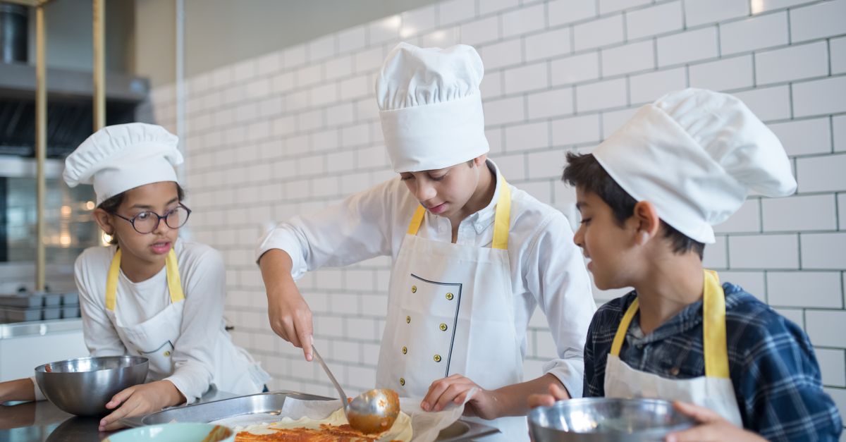 Young aspiring chefs in Portugal make pizza, spreading tomato sauce enthusiastically in a fun cooking class.