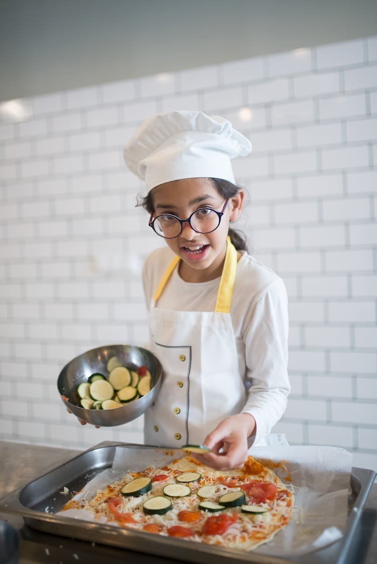 A Young Girl Putting Toppings On A Pizza