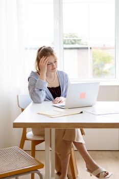 A stressed young woman working on a laptop at home office during the day.
