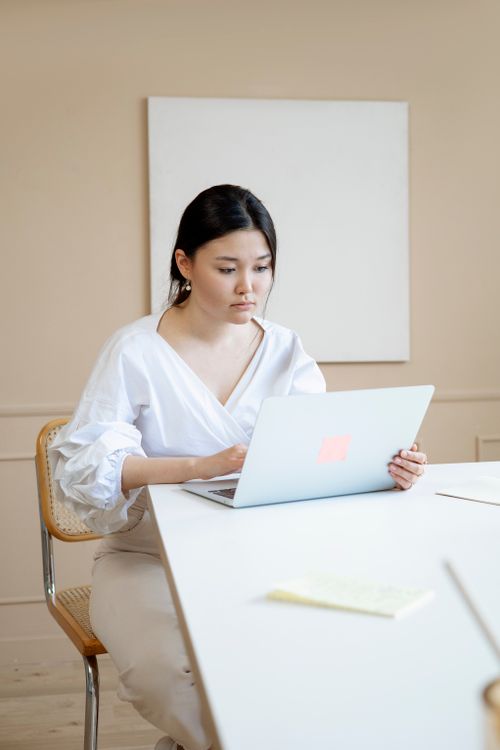 Free Young professional woman focused on her work using a laptop in a modern and minimalist office setting. Stock Photo