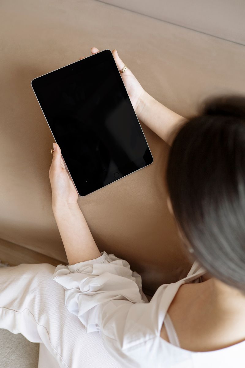 A woman is sitting and holding a digital tablet indoors.