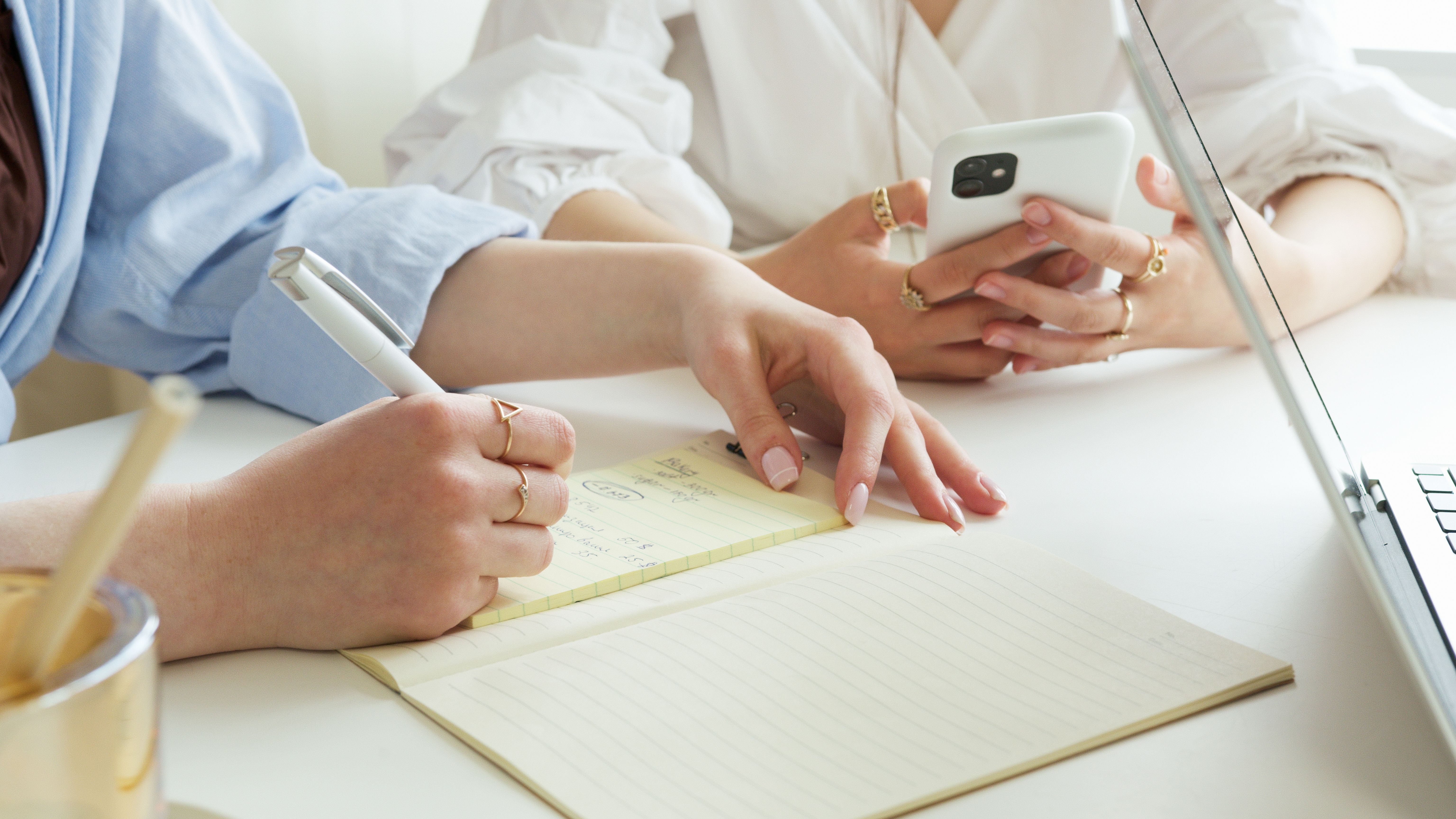 Women collaborating in a workspace with a notebook and smartphone, focusing on productivity.