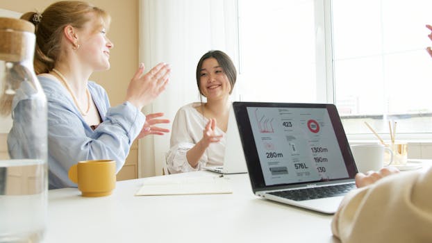 A group of professionals discussing project details around a table with a laptop showing data.