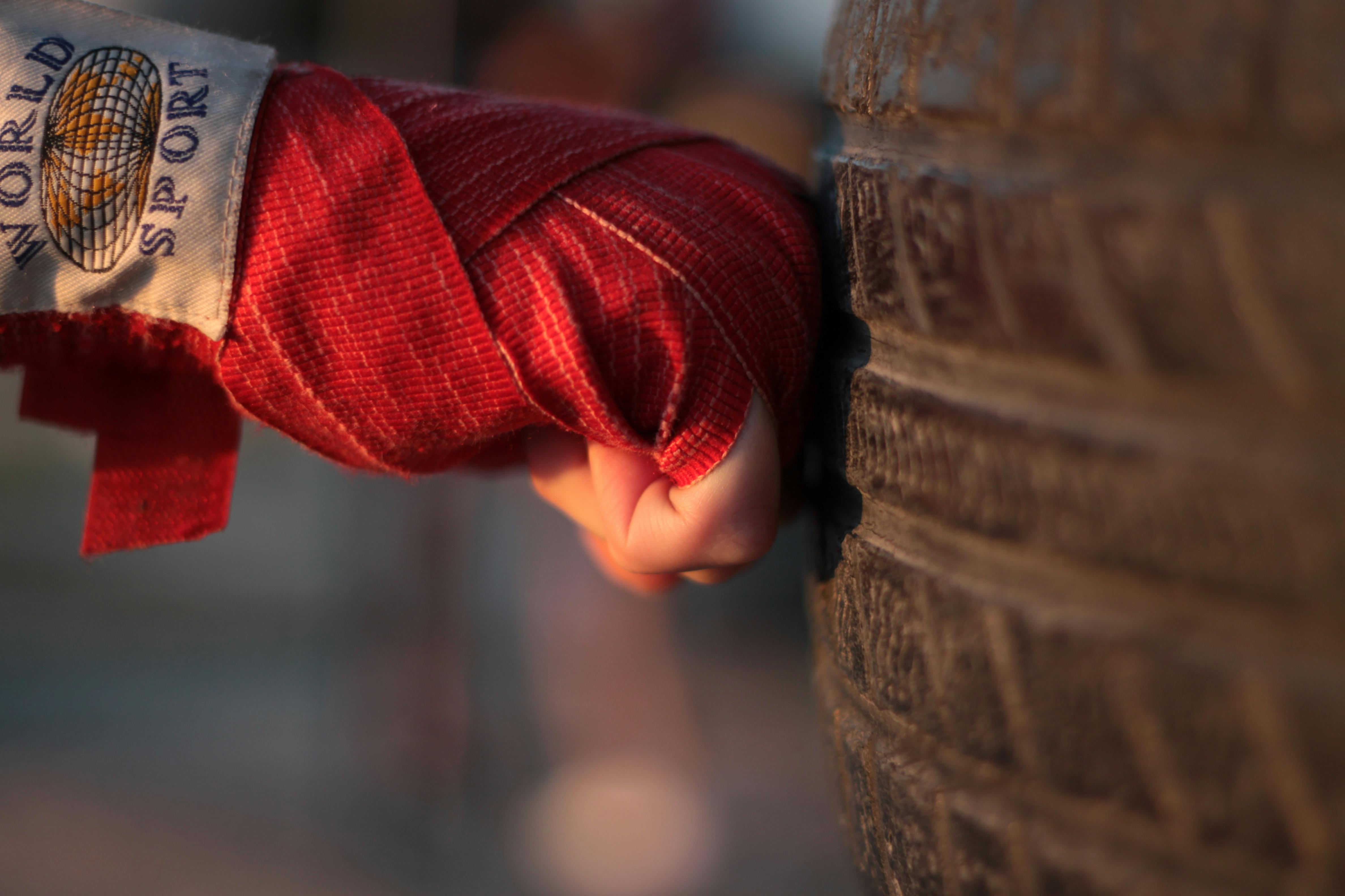 Boxer's hand wrapped in red bandage striking a tire, emphasizing training intensity.