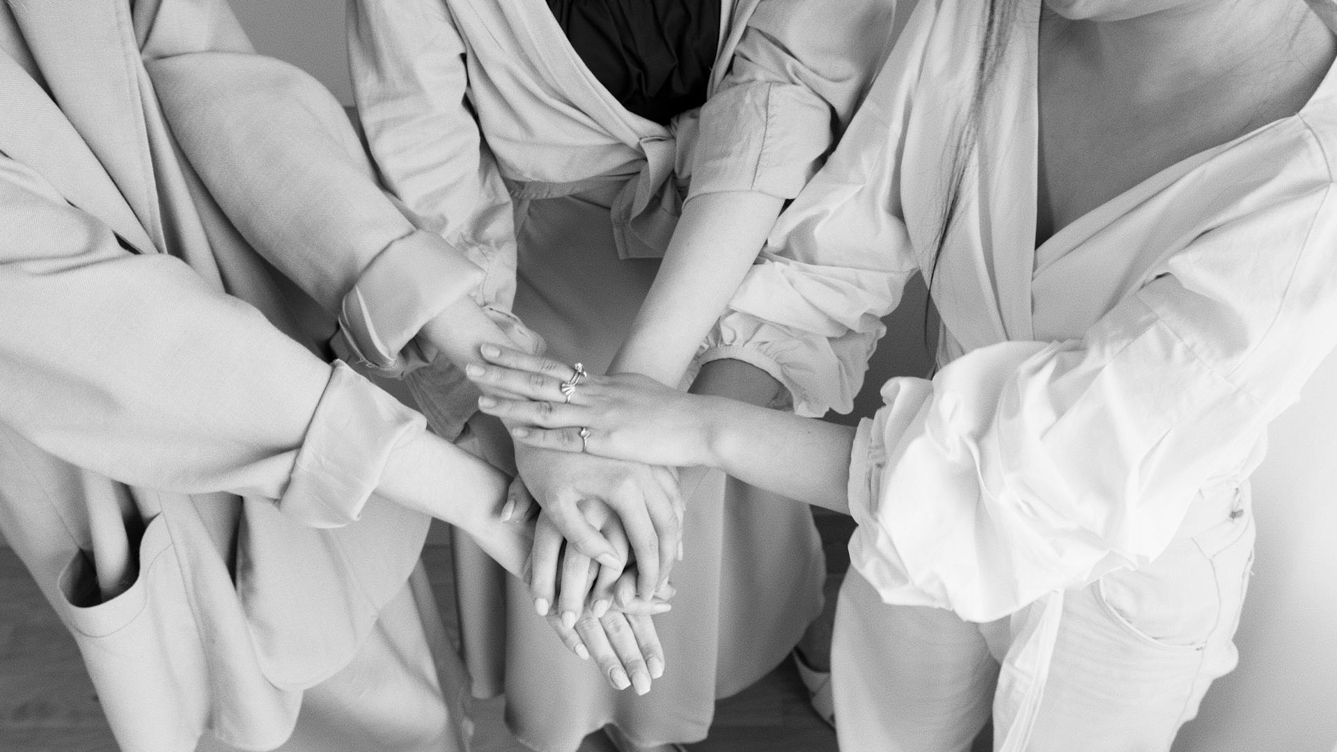 Black and white image of diverse hands stacked in teamwork gesture.