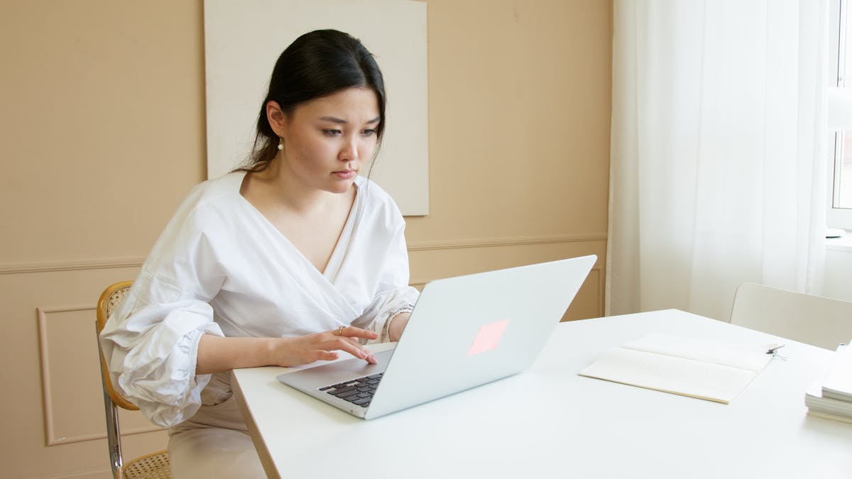 Woman in white top working on a MacBook Air, focused while using laptop at a desk