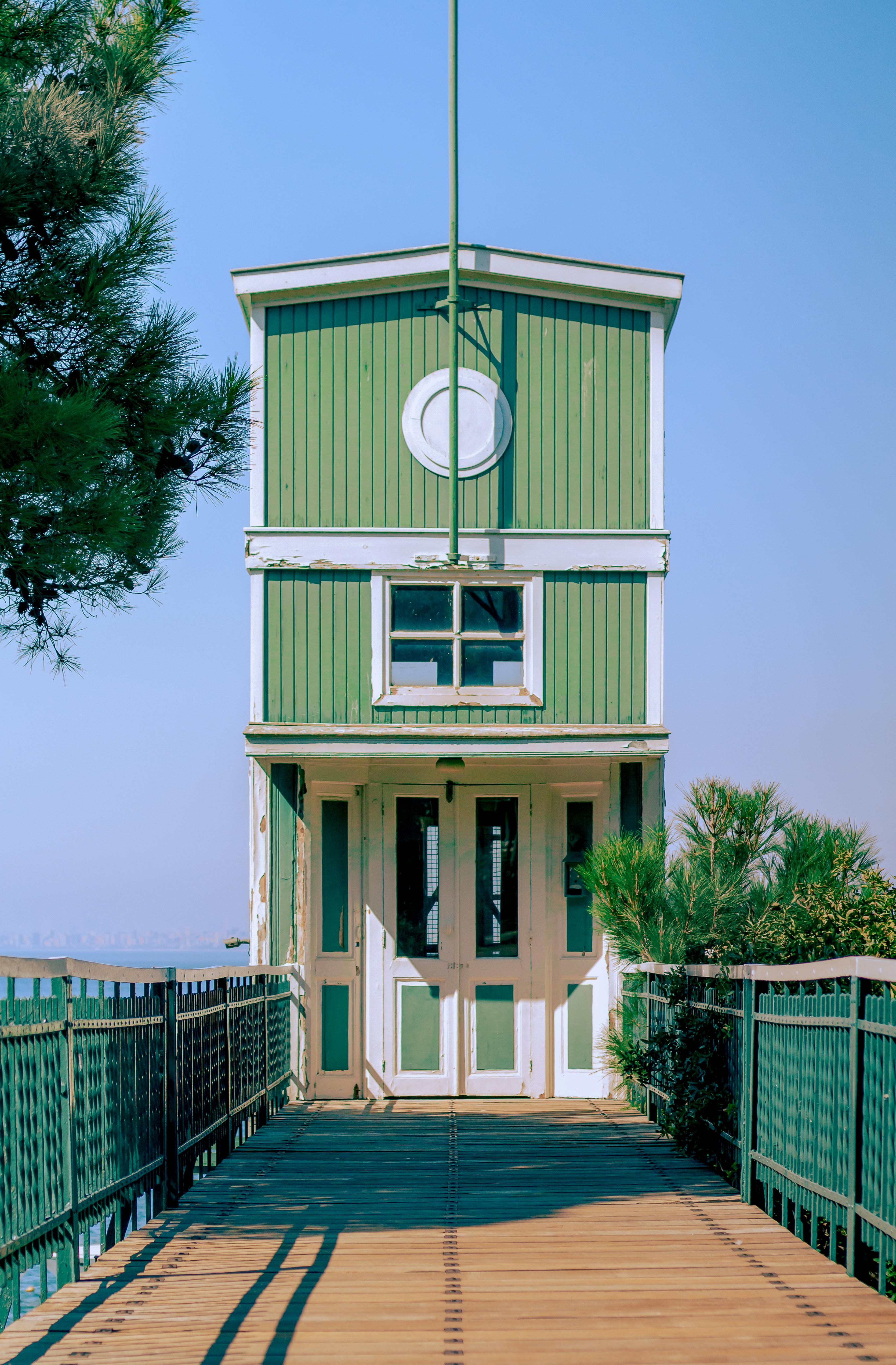 A picturesque green beach house with a wooden bridge and clear blue sky.