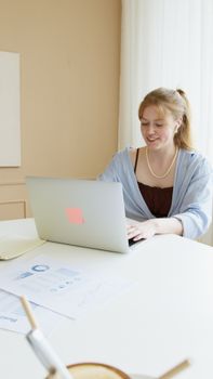 Smiling young woman working on a laptop at her desk in a bright, modern office setting.