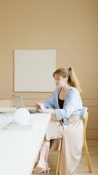 A young woman is working on a laptop at a minimalist desk in a bright, modern office setting.