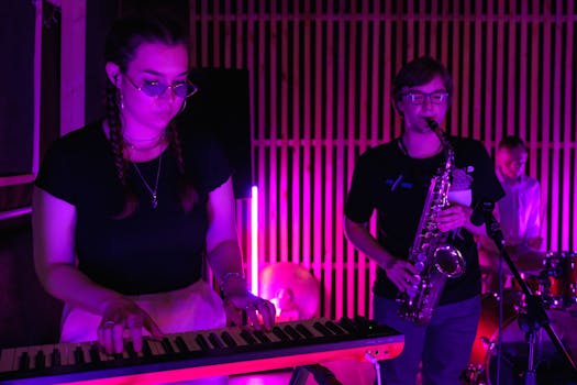 A band performing live music with a keyboard and saxophone under colorful stage lighting.