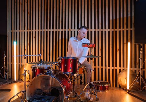 Young man playing drums in a modern studio setting. Musical performance captured with dynamic lighting.