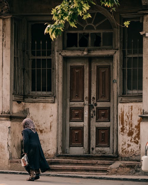 Woman Walking Past an Old Abandoned House
