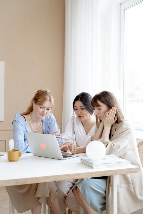 Free Three women collaborating on a laptop in a modern office setting, promoting teamwork and diversity. Stock Photo
