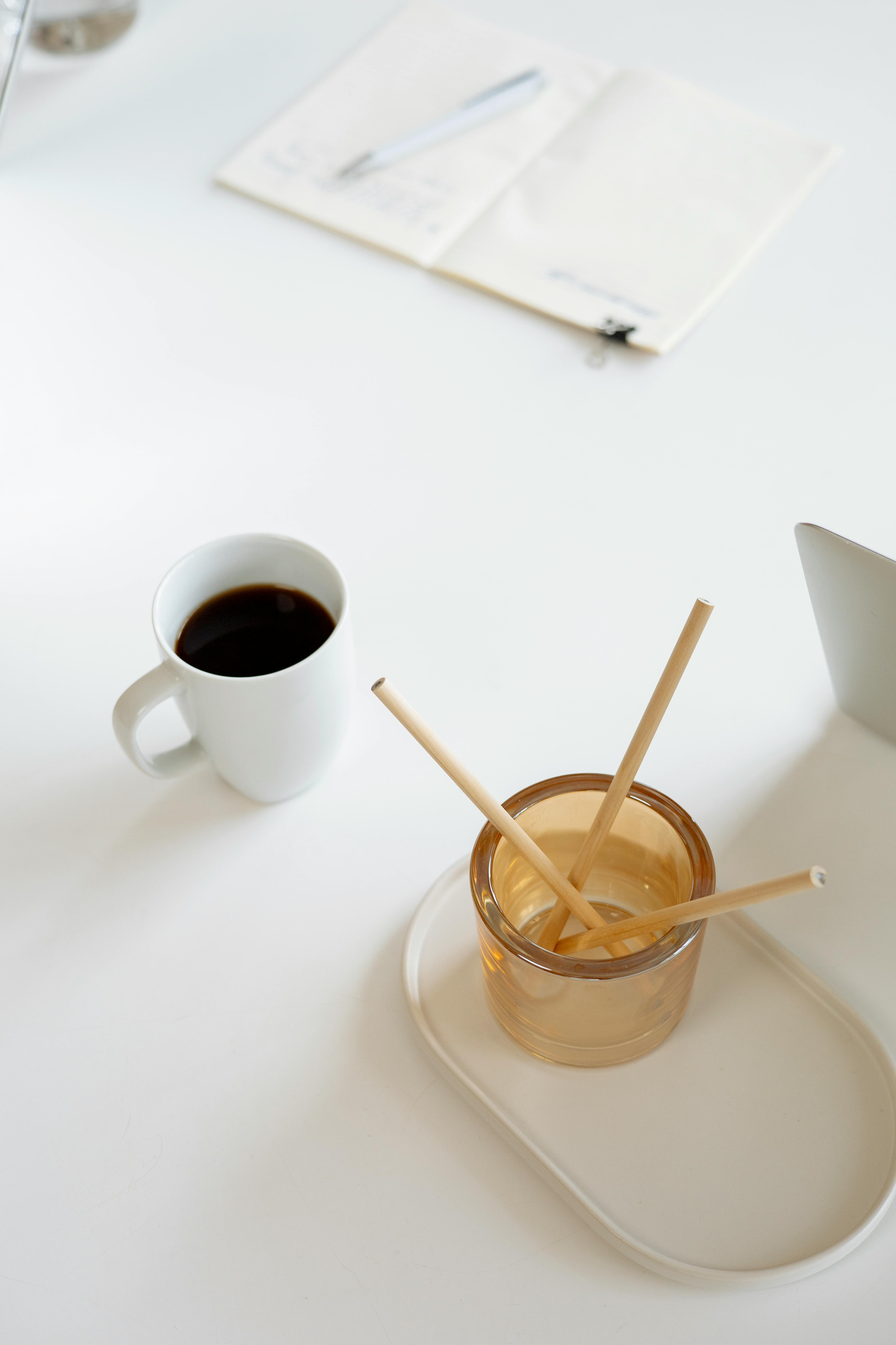 A clean, minimalist office desk setup featuring a coffee cup, straws, and an open notepad, creating a focused work environment.