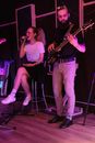 Woman in White Shirt Singing Beside a Man Using a Guitar