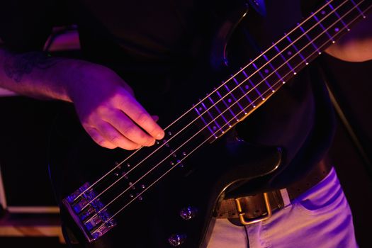 Close-up of a musician's hands skillfully playing a black electric bass guitar.