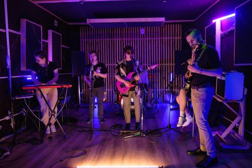 Free A dynamic live band performing with musical instruments in a neon-lit room. Stock Photo
