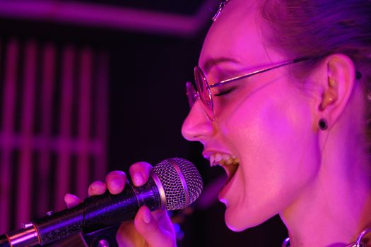 A vibrant close-up of a female singer performing with passion under purple stage lights.