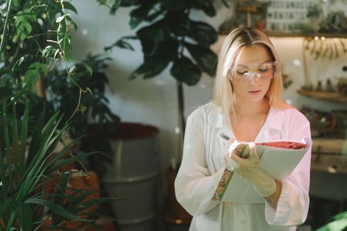 Free Focused female botanist writing down observations in a laboratory surrounded by plants. Stock Photo